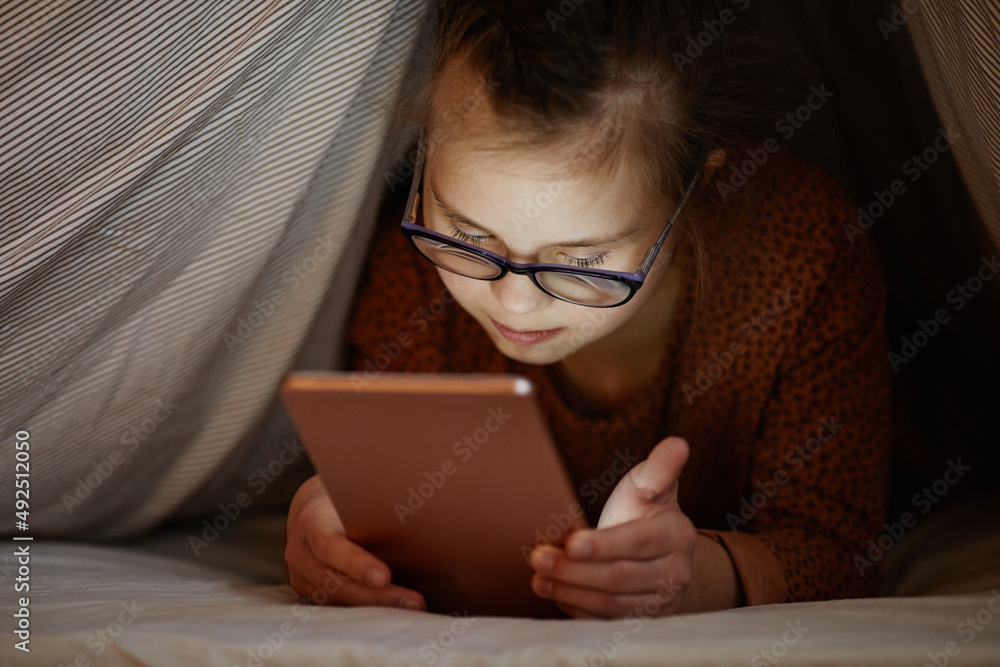 Obraz premium Portrait of young girl with down syndrome using smartphone in bed hiding under covers, digital obsession
