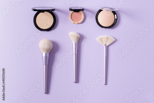 Makeup brushes for blush, highlighter and powder on purple background. Applying of makeup brushes. Cosmetic, professional brushes kit. Flat lay