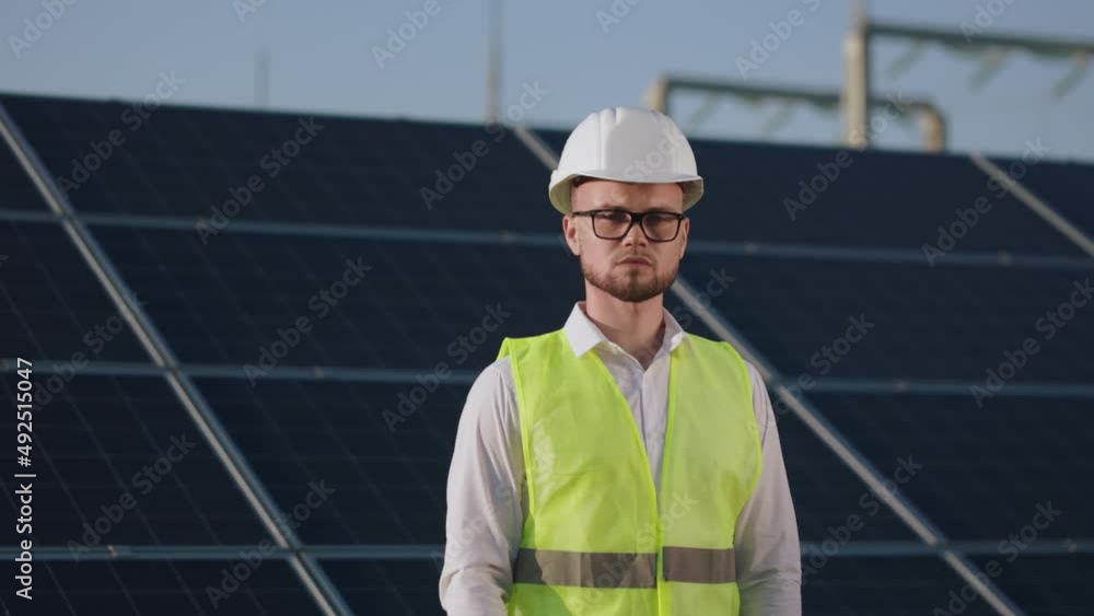 Portrait of confident caucasian man putting on safety white helmet while standing at solar station and looking at camera. Alternative energy concept. Portrait of confident caucasian man putting on safety white helmet while standing at solar station and looking at camera. Alternative energy concept.