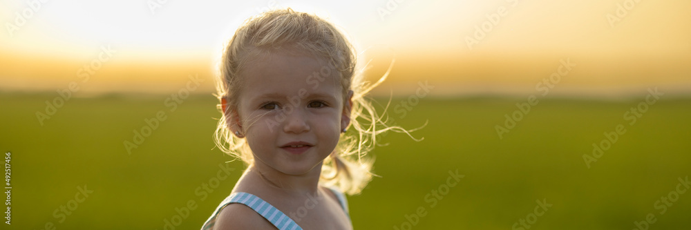 Retrato apaisado de niña de dos años en el campo al atardecer. Brisa veraniega.