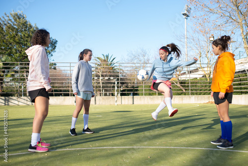 Joyful school girls enjoying playing football outdoors. Four Caucasian girls in sportswear exercising with ball on stadium training kicking and passing to each other. Healthy lifestyle, sport concept