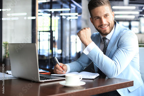 Portrait of happy businessman sitting at office desk, looking at camera, smiling photo