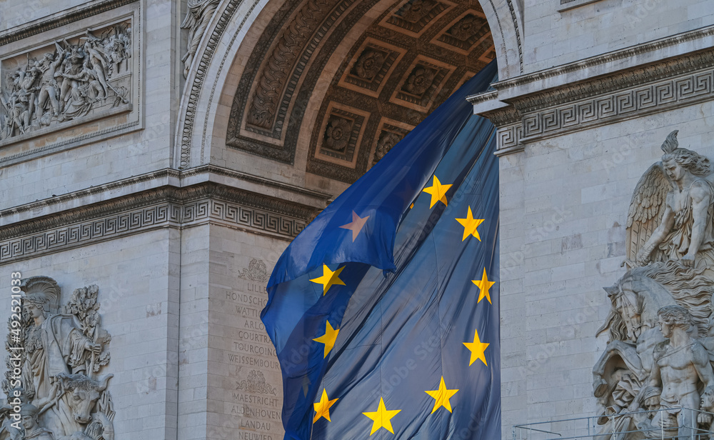 Flag of the European Union winding under the landmark Arch of Triumph building in Paris, France, during a beautiful sunrise.