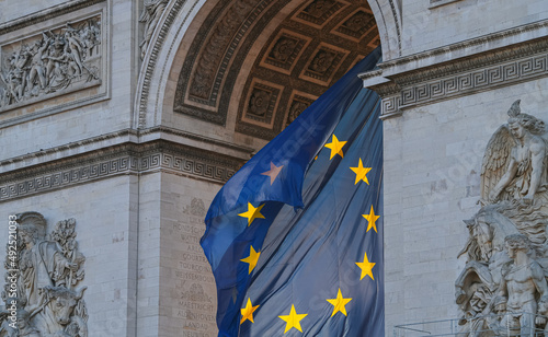 Flag of the European Union winding under the landmark Arch of Triumph building in Paris, France, during a beautiful sunrise.