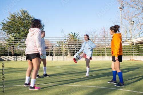 Sporty girls playing football on stadium. Four Caucasian girls in sportswear training focused on playing ball kicking it and improving skills for new games. Healthy lifestyle and team sport concept