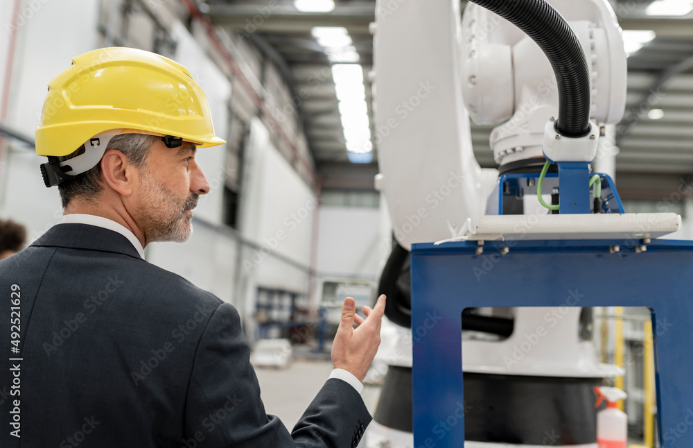 Engineer analyzing robotic arm standing in factory Engineer analyzing robotic arm standing in factory