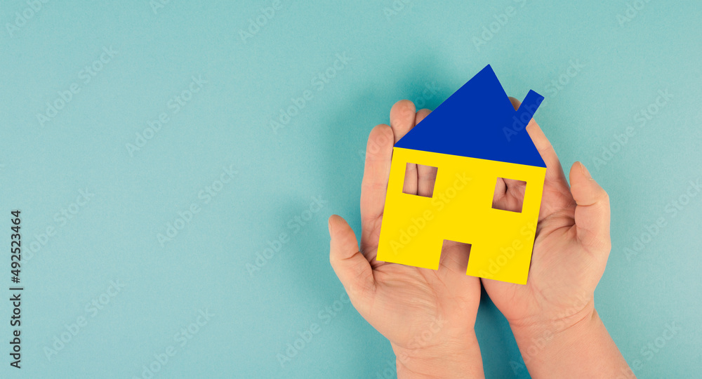Holding a house in the hand with the colors of the ukrainian flag, home for refugees from Ukraine, help for families Holding a house in the hand with the colors of the ukrainian flag, home for refugees from Ukraine, help for families