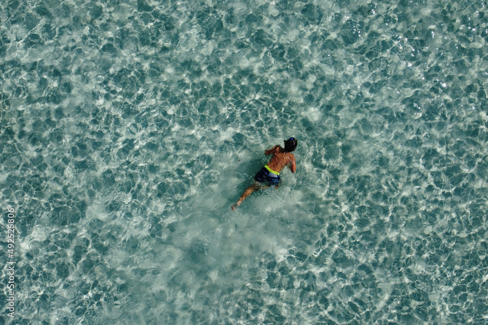 Little kid snorkeling on a turquoise ocean. Aerial view