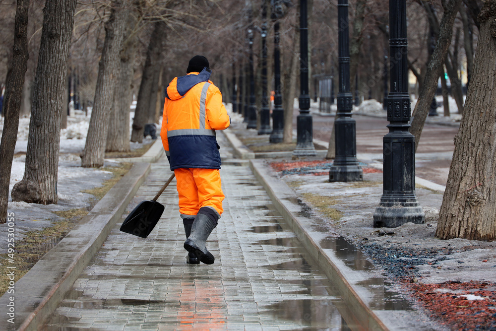 Cleaning street in a city, janitor with shovel removes melting snow in spring park. Work of housing and communal services Cleaning street in a city, janitor with shovel removes melting snow in spring park. Work of housing and communal services