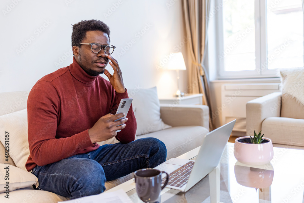 African astonished man sitting on sofa holds cellphone read e-mail sms feels shocked received terrified news, guy looks at online calendar forgot missed important meeting, phone problems concept..