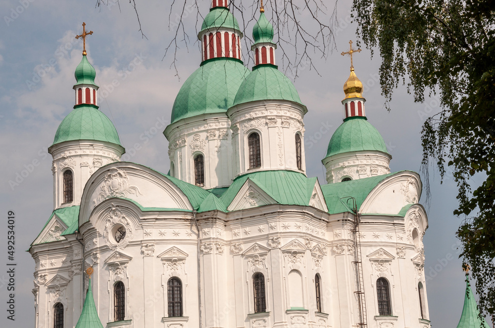 Christian orthodox white church with green domes with gold crosses. Calm blue sky above