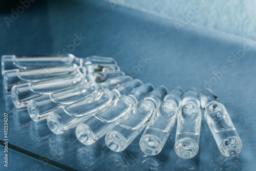 Glass medical ampoule vial for injection. Medicine is liquid sodium chloride with of aqueous solution in ampulla. Close up. Bottles ampule multicolor on background color and water. Human plasma.