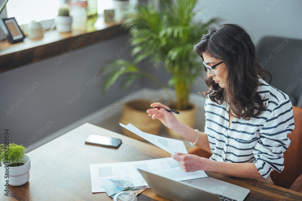 A beautiful black-haired businesswoman sitting in her home office and filling out bills. Busy business woman. The concept of finance A beautiful black-haired businesswoman sitting in her home office and filling out bills. Busy business woman. The concept of finance