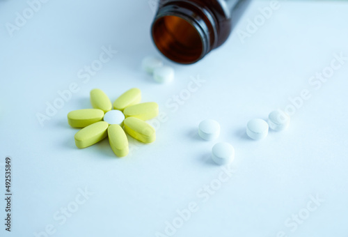 Vitamins for women are white, yellow. They are laid out in the shape of a flower on a white background with a brown bottle. The concept of an active lifestyle.