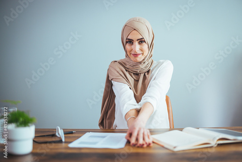Entrepreneurship For Islamic Women. Portrait of happy muslim businesswoman in hijab with papers at home office workplace, copy space