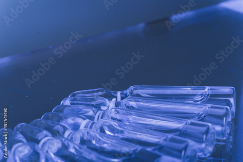 Glass medical ampoule vial for injection. Medicine is liquid sodium chloride with of aqueous solution in ampulla. Close up. Bottles ampule multicolor on background color and water. Human plasma.