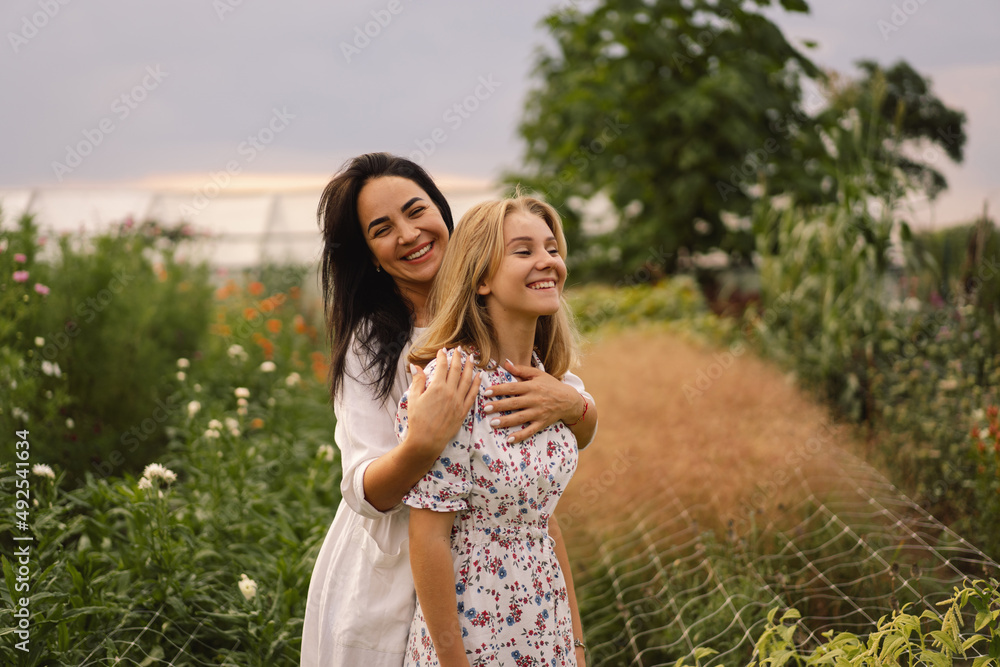 Obraz premium Happy mother's day. A young mother with a teenage daughter spends time in the garden. Mom and her daughter teenage girl are playing, smiling and hugging. Loving single mother hugs cute daughter.