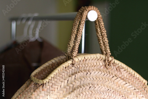 Straw bag and neutral clothes on a clothing bag. Selective focus.