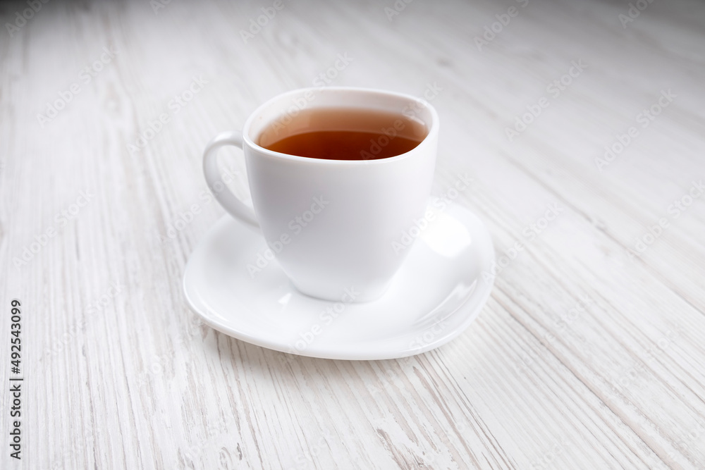 White cup with black tea on a wooden table, side view