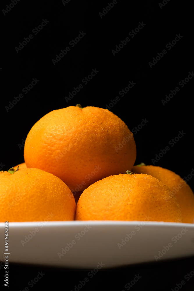 Close-up of ripe juicy sweet tangerines with drops of water lying in a white plate on a black background. Vertical photo Close-up of ripe juicy sweet tangerines with drops of water lying in a white plate on a black background. Vertical photo