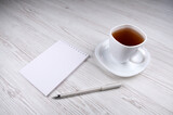 White pen, notepad and white cup of tea on a wooden table
