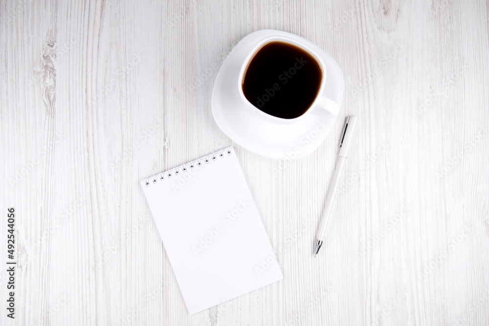 White cup of coffee, notepad and white pen on a wooden table, top view White cup of coffee, notepad and white pen on a wooden table, top view