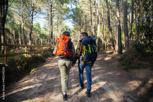 Back view of fond couple of young hikers. Caucasian man with beard and woman with dark hair with big backpacks holding hands. Hobby, nature, love concept