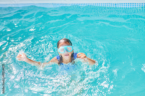 Little girl in goggles having fun, dives and swim in the swimming pool