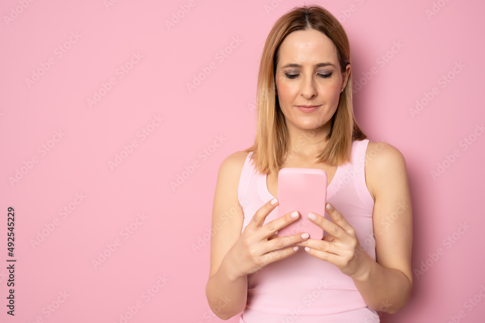 Happy young woman using smartphone standing isolated over pink background. Happy young woman using smartphone standing isolated over pink background.