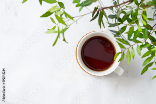 A cup of tea on a light marble background with green branches close-up. Spring women's concept. Front view and copy space