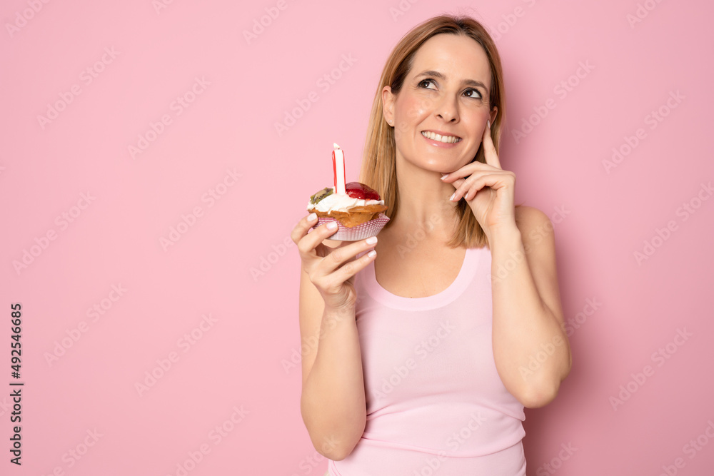 Image of happy woman in casual clothes holding piece of birthday cake with candle isolated over pink background. Celebration concept. Image of happy woman in casual clothes holding piece of birthday cake with candle isolated over pink background. Celebration concept.