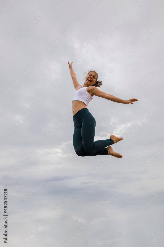 Slim Caucasian young woman jumping over cloudy sky. Caucasian woman wearing sportswear. Fitness, sport, wellness concept. Outdoor activity. Copy space. Sky background. Bali Slim Caucasian young woman jumping over cloudy sky. Caucasian woman wearing sportswear. Fitness, sport, wellness concept. Outdoor activity. Copy space. Sky background. Bali