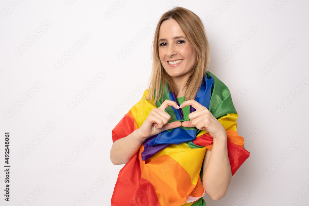 Happy woman posing with rainbow LGBT flag showing heart figure with fingers standing isolated over white background. Happy woman posing with rainbow LGBT flag showing heart figure with fingers standing isolated over white background.