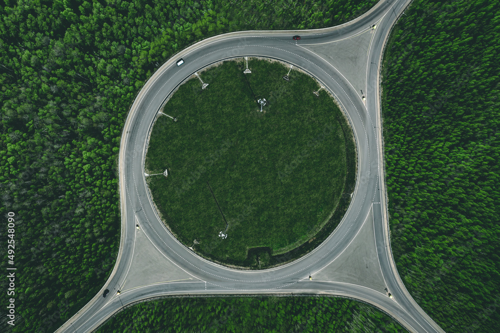 Aerial view of a traffic roundabout and road junctions in green forest - obrazy, fototapety, plakaty 