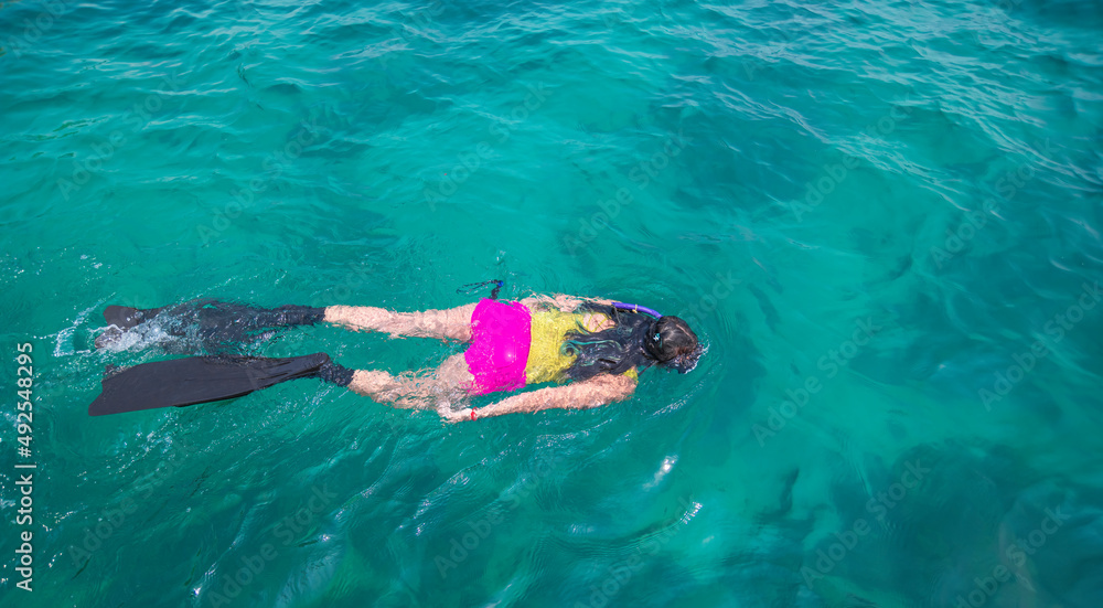 Beautiful sport woman wearing swimming suite under free diver glides over sandy sea with scuba and fins. Woman free diver in summer holiday.