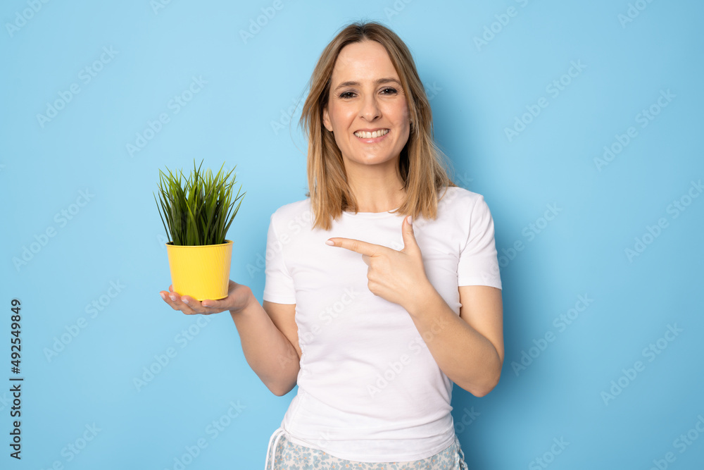 Young beautiful woman holding pot over blue isolated background with a happy face standing and smiling with a confident smile showing teeth Young beautiful woman holding pot over blue isolated background with a happy face standing and smiling with a confident smile showing teeth