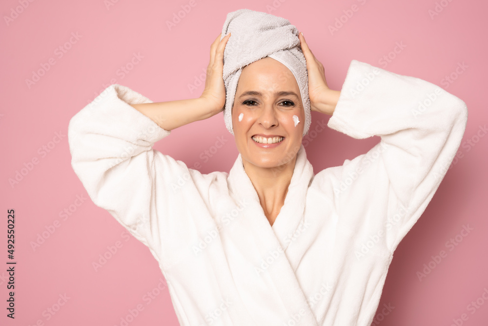 Happy young woman in bathrobe with cream in her face standing isolated over pink background. Beauty concept. Happy young woman in bathrobe with cream in her face standing isolated over pink background. Beauty concept.