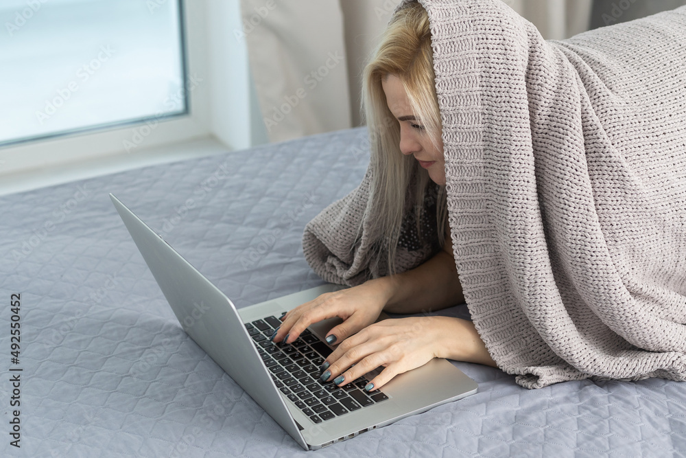 woman using laptop covered with blanket at the bedroom woman using laptop covered with blanket at the bedroom