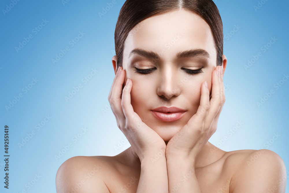 Young woman with natural makeup and smooth skin against light blue background Young woman with natural makeup and smooth skin against light blue background