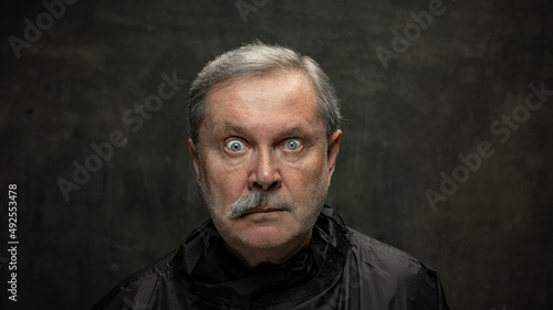 Portrait of surprised senior man looking at camera isolated on dark vintage background. Concept of emotions, fashion, beauty, self-reinvention