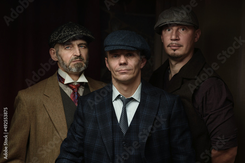 Three men of different ages, an English retro gangster of the 1920s, dressed in a coat, suit and flat cap photo