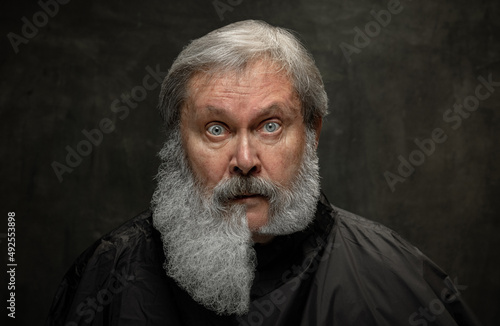 Composite image made of portrait of shocked grey-bearded senior man looking at camera isolated on dark vintage background.