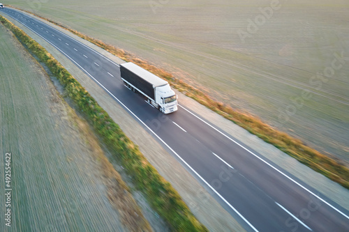 Aerial view of blurred fast moving semi-truck with cargo trailer driving on highway hauling goods in evening. Delivery transportation and logistics concept © bilanol