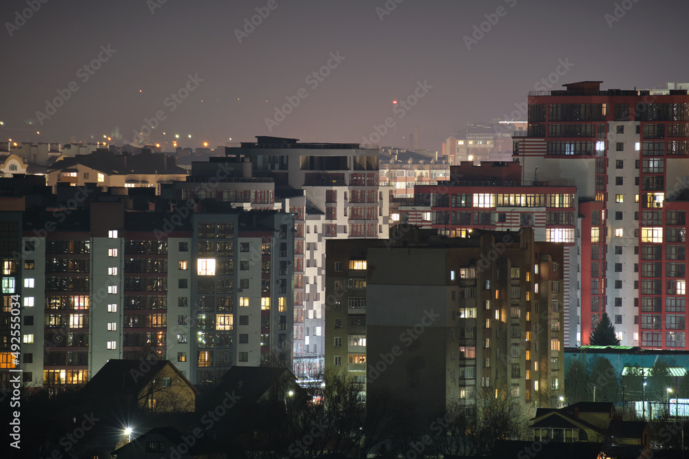 Architectural details of modern high apartment buildings with many illuminated windows and balconies at night