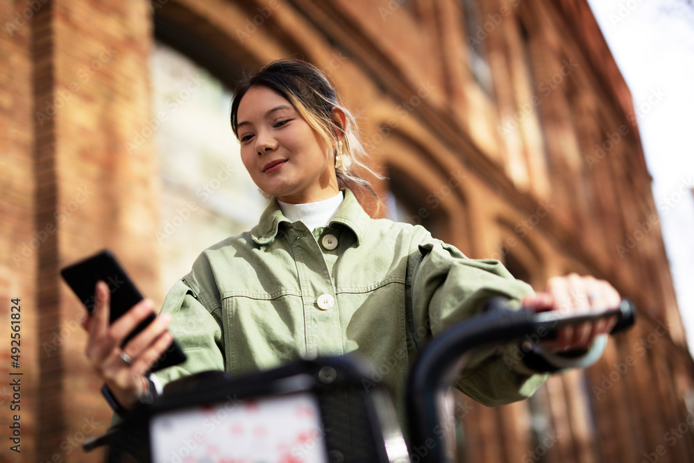 Fototapeta premium Young Chinese woman using the phone. Beautiful happy lady with electric bicycle..