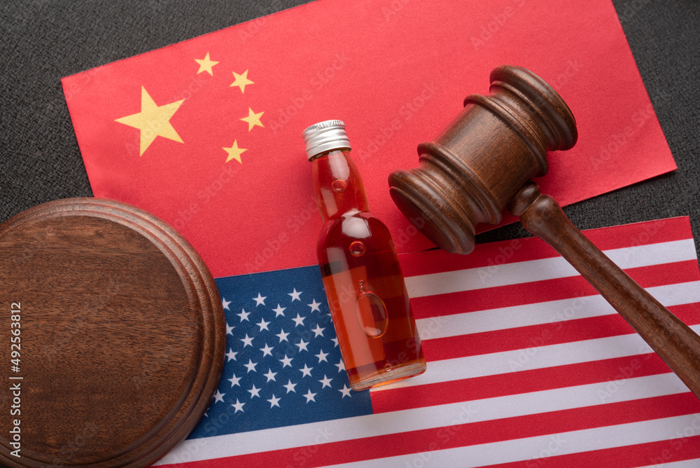 Bottle of alcohol and judge gavel on the flags of the United States and China. Alcohol Import Act. Duty on alcohol.
