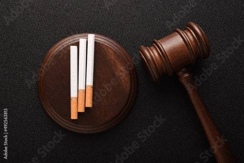 Cigarettes and wooden Judge gavel. Top view on black background. Violation of the terms of sale of tobacco. Tobacco law.