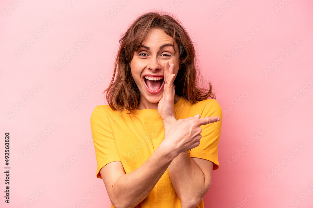 Young caucasian woman isolated on pink background saying a gossip, pointing to side reporting something. Young caucasian woman isolated on pink background saying a gossip, pointing to side reporting something.