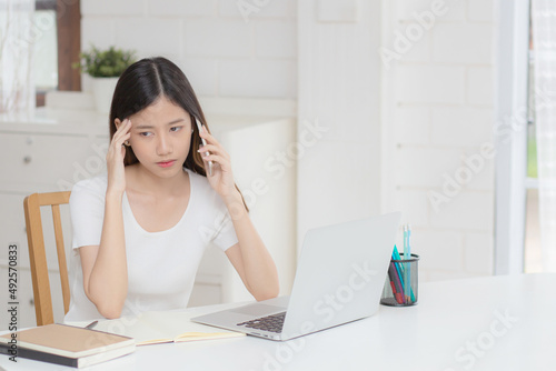 Obraz na plátne Young asian woman working on laptop computer and talking smartphone having stress and upset at home, girl having problem and worried, frustrated and unhappy, business and communication concept