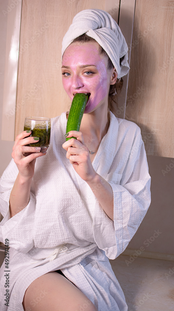 Funny young woman with facial cucumbers mask. Girl with face skincare mask eat fresh cucumber on beige background . Clean skin and beauty concept Funny young woman with facial cucumbers mask. Girl with face skincare mask eat fresh cucumber on beige background . Clean skin and beauty concept
